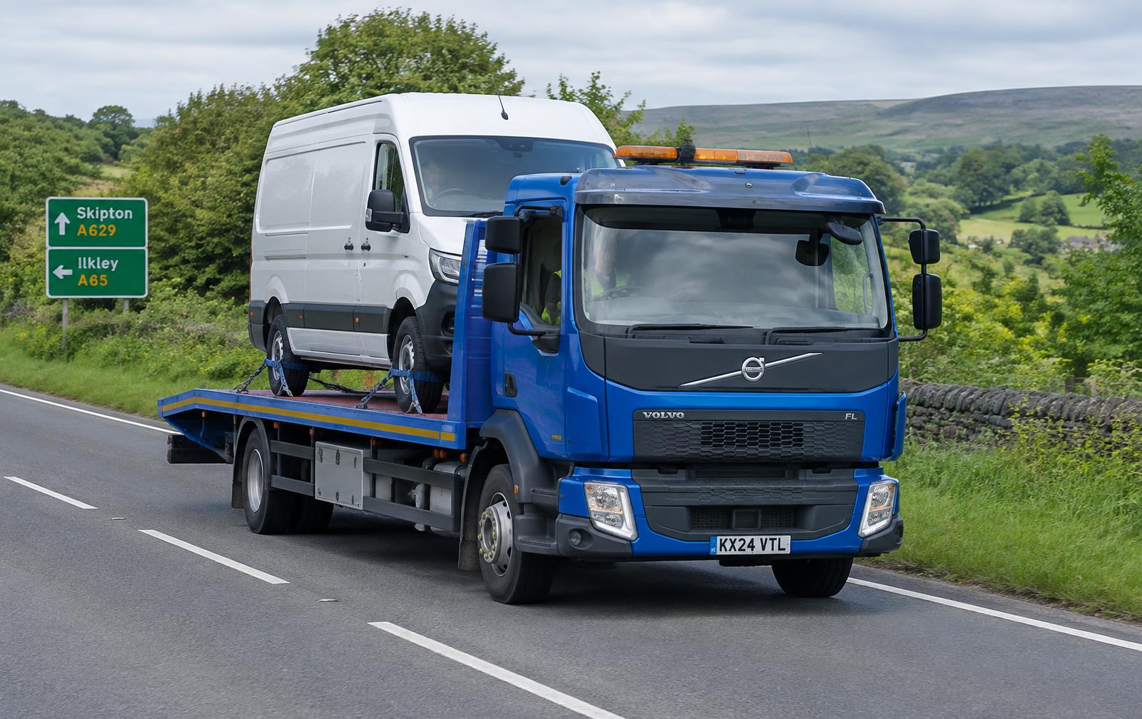 Blue flatbed transporter delivering a van on a UK road